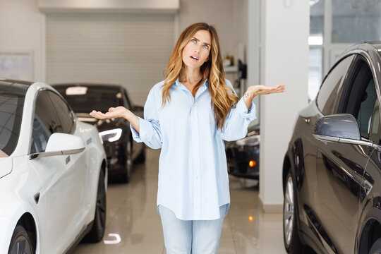 Uncertain woman customer female buyer client wears blue shirt chooses auto between two cars wants to buy new automobile in car showroom vehicle salon dealership store motor show indoor. Sales concept