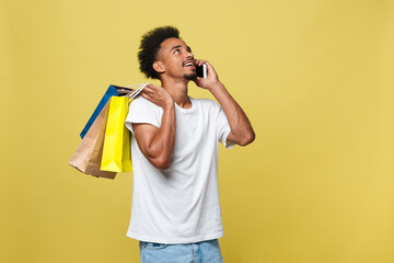 young man with shopping bags talking on smart phone isolated on yellow background