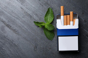 Pack of menthol cigarettes and mint on grey table, flat lay. Space for text