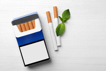 Menthol cigarettes, pack and mint on white wooden table, flat lay. Space for text