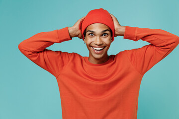 Fototapeta premium Young surprised shocked amazed happy cool smiling african american man 20s wearing red shirt hat hold head isolated on plain pastel light blue background studio portrait. People lifestyle concept