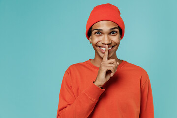 Young fun happy smiling secret african american man in red shirt hat say hush be quiet with finger...