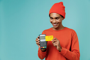 Young smiling cool african american man in orange shirt hat hold wireless modern bank payment...