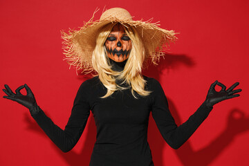 Young woman with Halloween makeup mask wears straw hat black scarecrow costume hold hands yoga om...