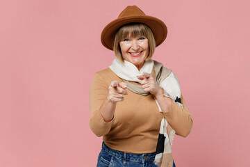 Traveler tourist leader senior lady woman 55 years old wears brown shirt hat scarf point index finger camera on you motivating encourage isolated on plain pastel light pink background studio portrait.