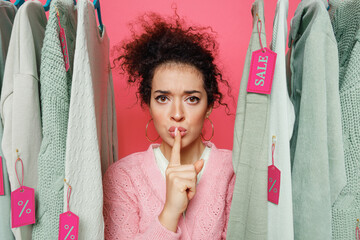 Young secret costumer woman 20s in sweater stand near clothes rack with tag sale in store showroom...