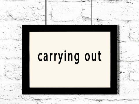 Black frame hanging on white brick wall with inscription carrying out