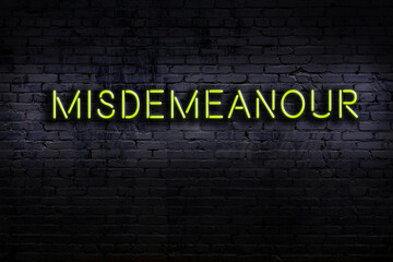 Neon sign. Word misdemeanour against brick wall. Night view