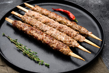 Shish kebab on a stick, from ground land mutton meat, on plate, on black dark stone table background