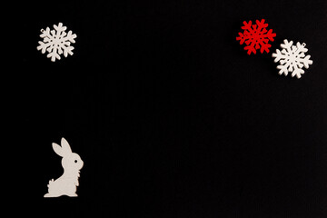 Stylish christmas composition on a black background, wooden figurines of hare, and snowflakes, copy space