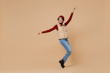 Fototapeta na wymiar Full body young woman 20s wears red turtleneck vest beret stand on toes leaning back with outstretched hands dancing fooling around have fun isolated on plain pastel beige background studio portrait