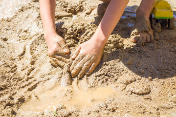 Barefeet kid playing with wet sand. Little boy kneads and models mud on summer sunny day