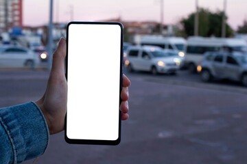 Mockup image of woman holding blank white screen mobile phone with blurry city background.