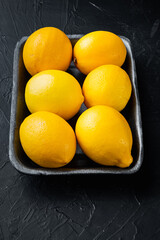 Fresh lemons, in plastic tray, on black background