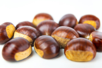 Ripe chestnuts, freshly picked and removed from the hedgehog, arranged on a white wooden surface.