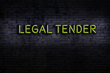 Night view of neon sign on brick wall with inscription legal tender