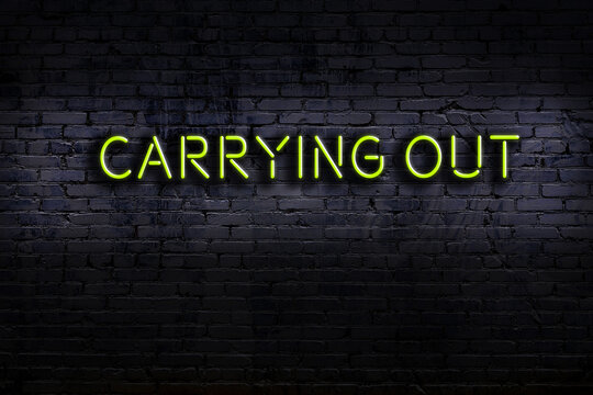 Neon sign. Word carrying out against brick wall. Night view