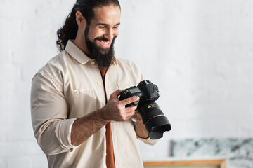 happy hispanic man smiling while looking at modern digital camera at home