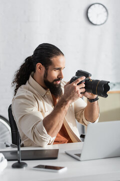 latin photographer taking picture on digital camera near blurred gadgets in home studio