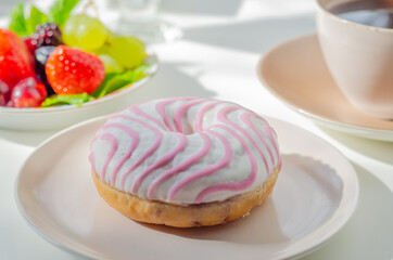 Delicious doughnut topped with white and pink icing served with coffee and fresh fruits