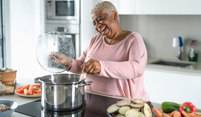 Happy senior woman having fun preparing lunch in modern kitchen - Hispanic Mother cooking for the...