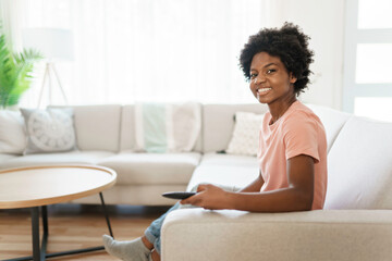 Fototapeta na wymiar Cheerful cute woman sitting on sofa in bright living room changing tv channel