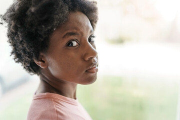 Pensive sad young African American woman look in window
