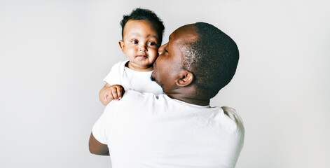portrait of beautiful african man holding on hands her little son on grey background