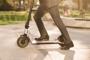 Close up of legs man in suit riding electric scooter in city. Unknown businessman in classic suit ride on electric mobile scooter. Modern eco friendly transport. Fast speed driving electric transport