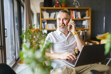 Businessman sitting at desk in bright office, talking on mobile phone