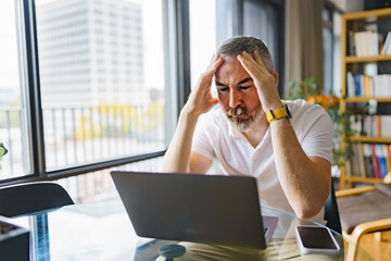 Businessman sitting at desk in bright office using laptop with sad attitude