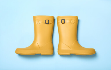 Pair of yellow rubber boots on light blue background, top view