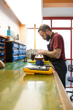 Concentrated man repairing guitar on table near multimeter in workshop