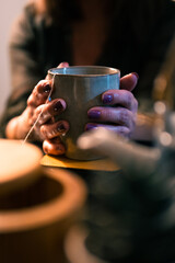 Fototapeta na wymiar Female hands holding cup of tea. The background is out of focus and the woman is unrecognizable. The woman is middle-aged. The atmosphere is warm and comfortable.