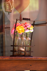 Artificial pink and yellow buttercup flowers in three small bottles in a rusty support on the chalet window