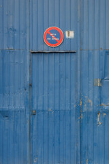 Postão metálico antigo de armazém em zona industrial, com aspeto abandonado e danificado, pintado na cor azul e com o sinal de trânsito de proibição de estacionar