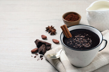 Yummy hot chocolate with cinnamon in cup on white wooden table. Space for text