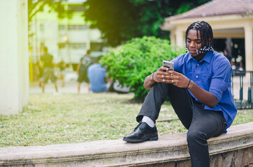 young latino dominican man with dark skin and curly and braided hair in the city park in a blue...
