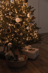 Christmas tree with gift boxes decorated with glowing garland lights, baubles. Christmas holidays celebration.