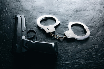 Black steel gun and Police metal real handcuffs lie on the black background. Private detective...