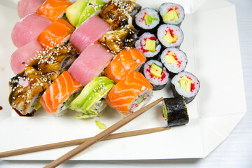 Man takes Tasty Colorful assorted Set of different type Sushi with chopsticks. Dinner in Japanese style. Healthy food. Filadelfia and Maki sushi rolls with Avocado, Tuna, Salmon, fish and Prawns.
