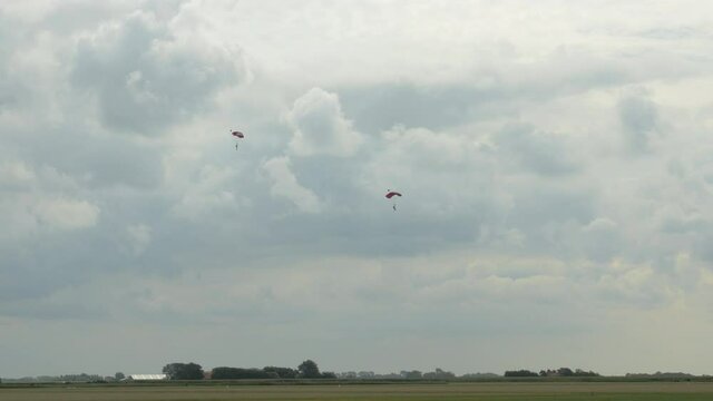 two single Skydivers with open Parachutes slowely glide down to earth. The scene is in the Netherlands on the Island of Texel during the summer.
