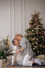 adult man and woman sit on the floor near the christmas tree and hug