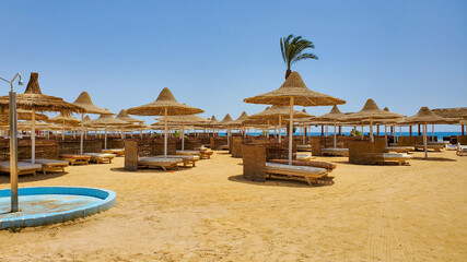 Sun loungers and straw umbrellas close-up on a sunny summer day on a sandy beach