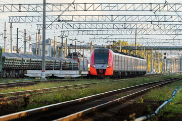 Obraz premium Front view of modern russian intercity high speed passenger train on railroad at sunset, freight train on background. Commercial suburban transportation concept