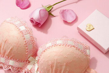 Top view of women's lingerie. Pink bra with gift box and beautiful flower on pink background. Romantic mood.