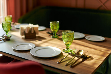 Table setting in the restaurant, white plates, green goblet, wooden table