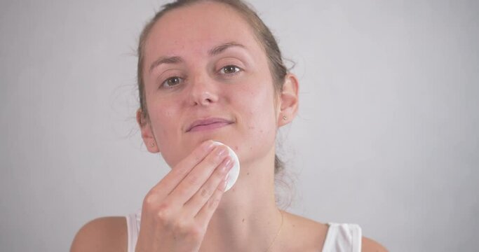woman removing her makeup with micellar water and a round cotton sponge