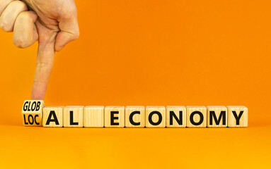 Local or global economy symbol. Businessman turns a wooden cube and changes words local economy to global economy. Beautiful orange background. Business, local or global economy concept. Copy space.