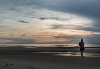 Young woman exercising on the sea beach at sunrise. Back view, Copy space, Focus and blur.